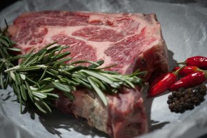 A peice of red meat on a plate with rosemary